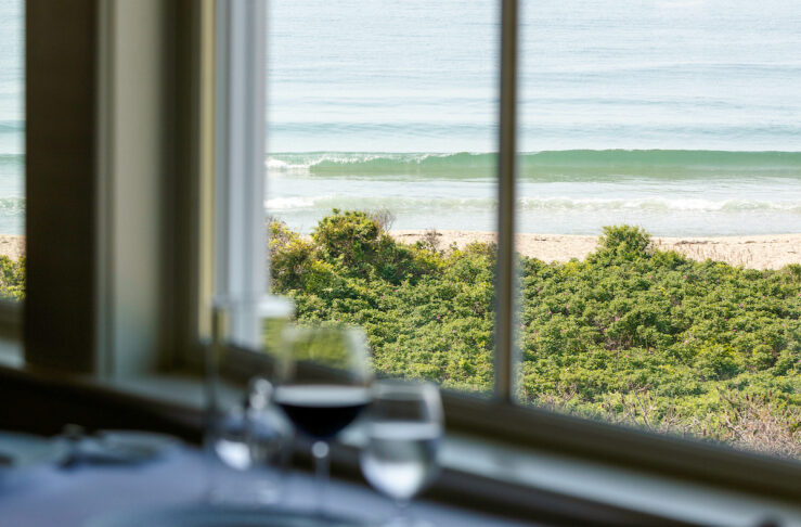 A window with an ocean view, and a set dining table in the foreground.